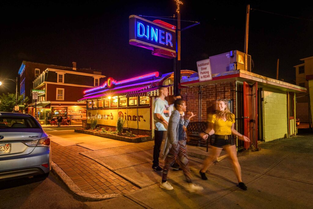 Students walking at night in front of the Boulevard Diver, illuminated by a vivid, neon sign.