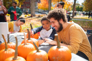 a student and a youngster paint pumpkins