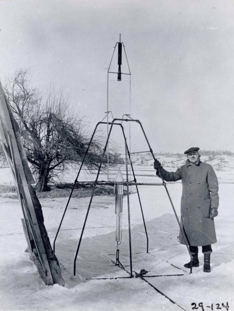 Robert Goddard standing in a field next to a rocket